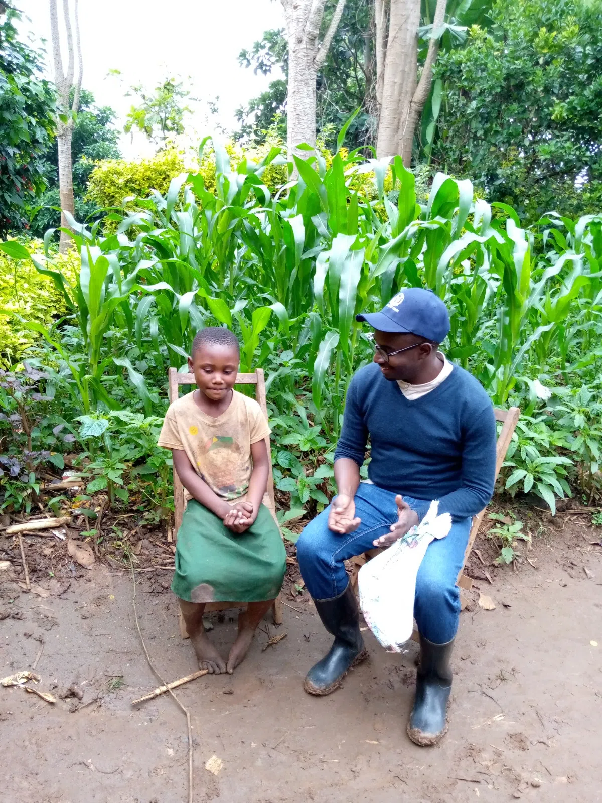 Claude, the founder of Imuhira ecotourism sitting next to a girl without shoes in a corn field